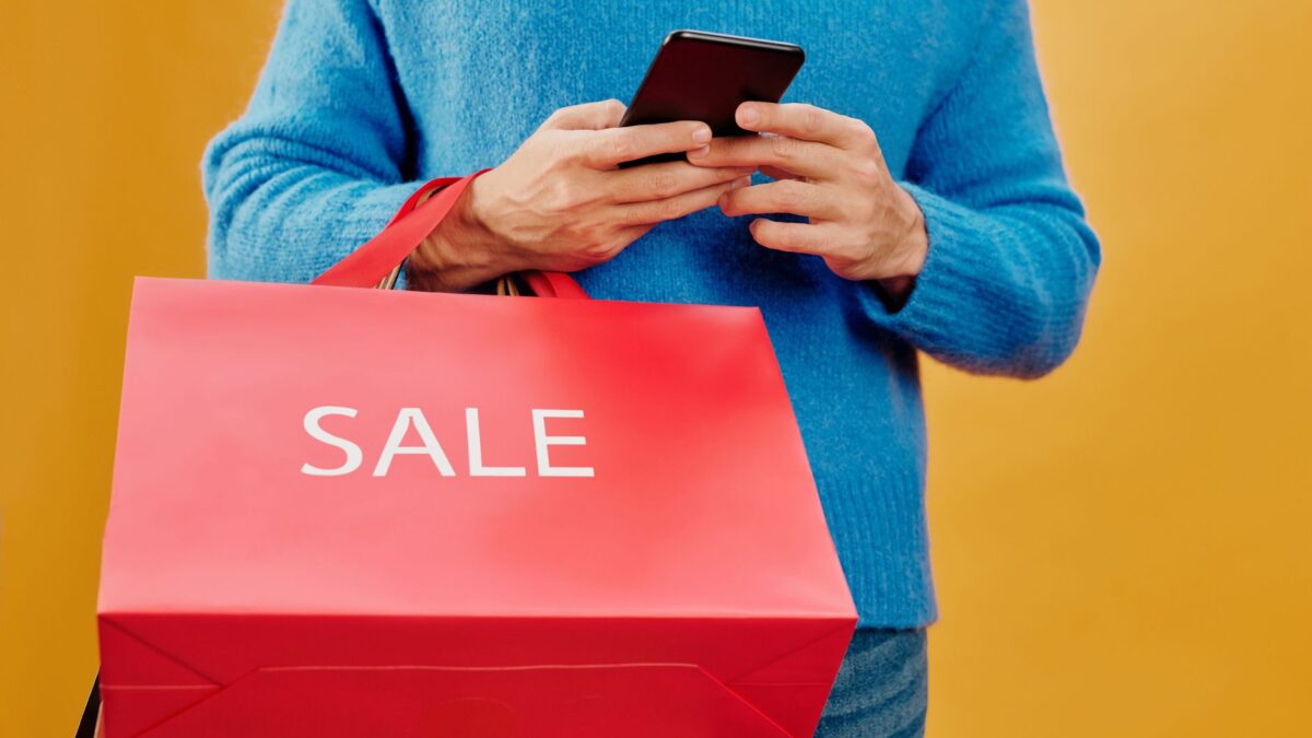 Osoba z telefonem i czerwoną torbą z napisem sale, ilustracja do tematu kampanii Meta Ads w sezonie wyprzedaży